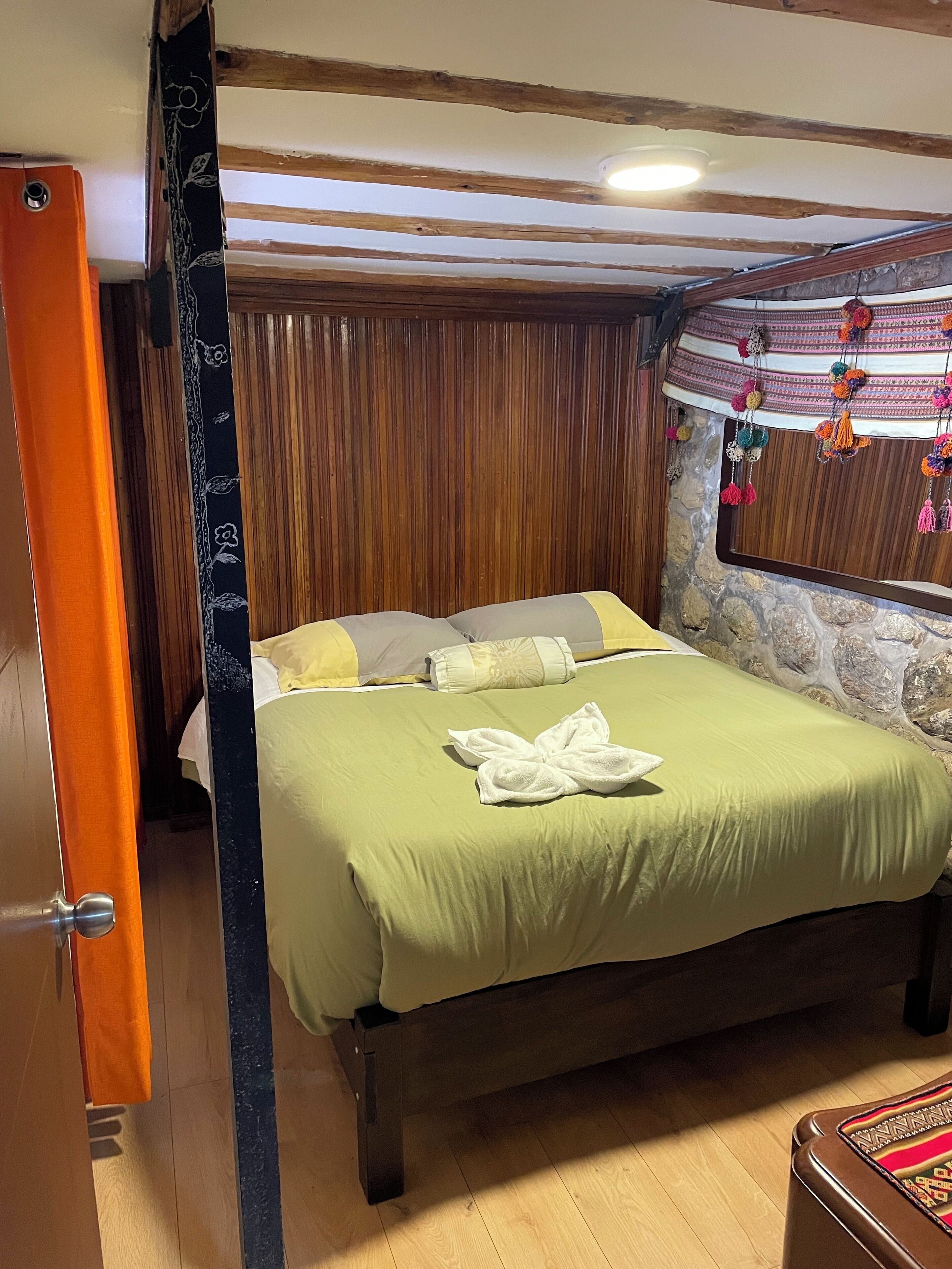 Une pièce avec un lit, des poutres en bois au plafond, un mur en pierre et une fenêtre décorée de guirlandes.