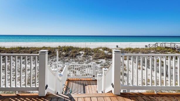 Un pontile di legno che conduce a una spiaggia, con ringhiere bianche e vista libera sull'oceano.