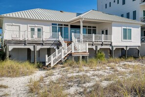 A beachfront house with a covered porch, a staircase leading to the main entrance, and a sandy beach in the foreground. - Direct Beach Access! Prime PCB Bungalow w/ Deck (Panama City Beach)
