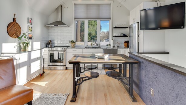 A modern kitchen with white cabinetry, a large window, a built-in oven, and a flat-screen TV mounted above the counter. - 2-Story Guesthouse w/ Private Deck in NE PDX (Portland)