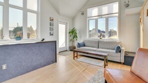 A spacious living room with a grey sofa, wooden coffee table, and a large window offering a view of the outside. - 2-Story Guesthouse w/ Private Deck in NE PDX (Portland)