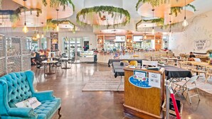 A spacious cafe with high ceilings, hanging plants, and a variety of seating options including a blue armchair and wooden tables. - 2026 Updated 2BR | Largest Lagoon Size Pool (Destin)