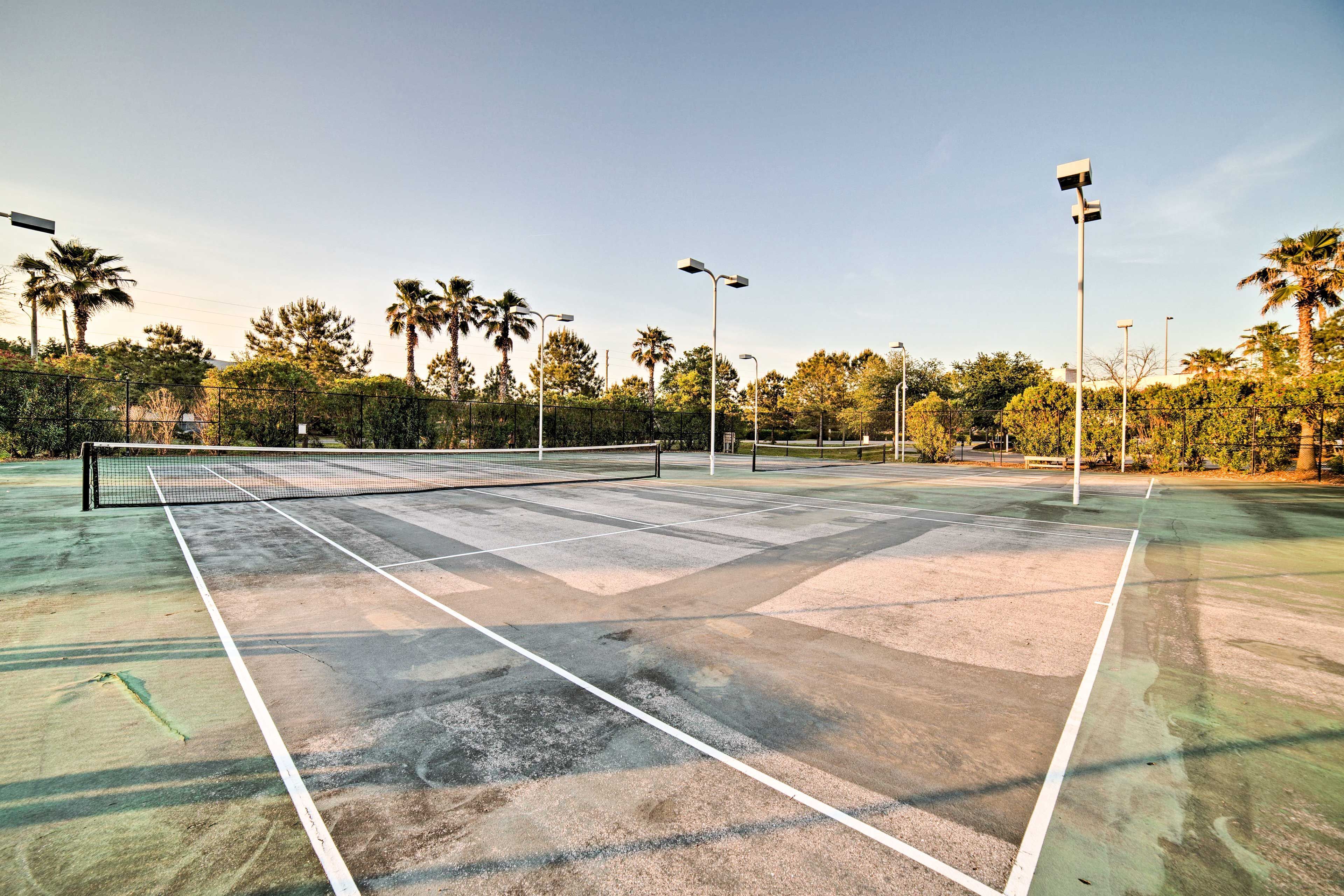An outdoor tennis court with a net, surrounded by trees and street lamps.