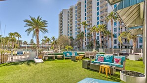 A rooftop pool area with outdoor seating, palm trees, and a high-rise building in the background. - 2026 Updated 2BR | Largest Lagoon Size Pool (Destin)