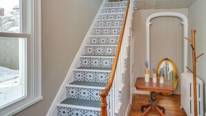 Una escalera con peldaños decorados y barandilla de madera, que lleva a una plataforma con un espejo y jarrones.