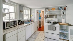 Una cocina compacta con gabinetes blancos, microondas, cafetera y estufa.