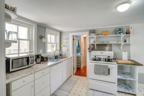 A compact kitchen with white cabinets, a microwave, a coffee maker, and a stove.