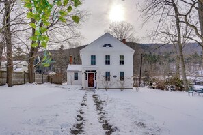 A white two-story house with a front porch, surrounded by snow-covered ground and trees. - Historic Family Retreat on the AT & Housatonic! (Lee)