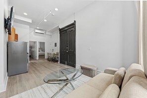 A modern living room with a glass coffee table, a sofa, and a kitchen area in the background.