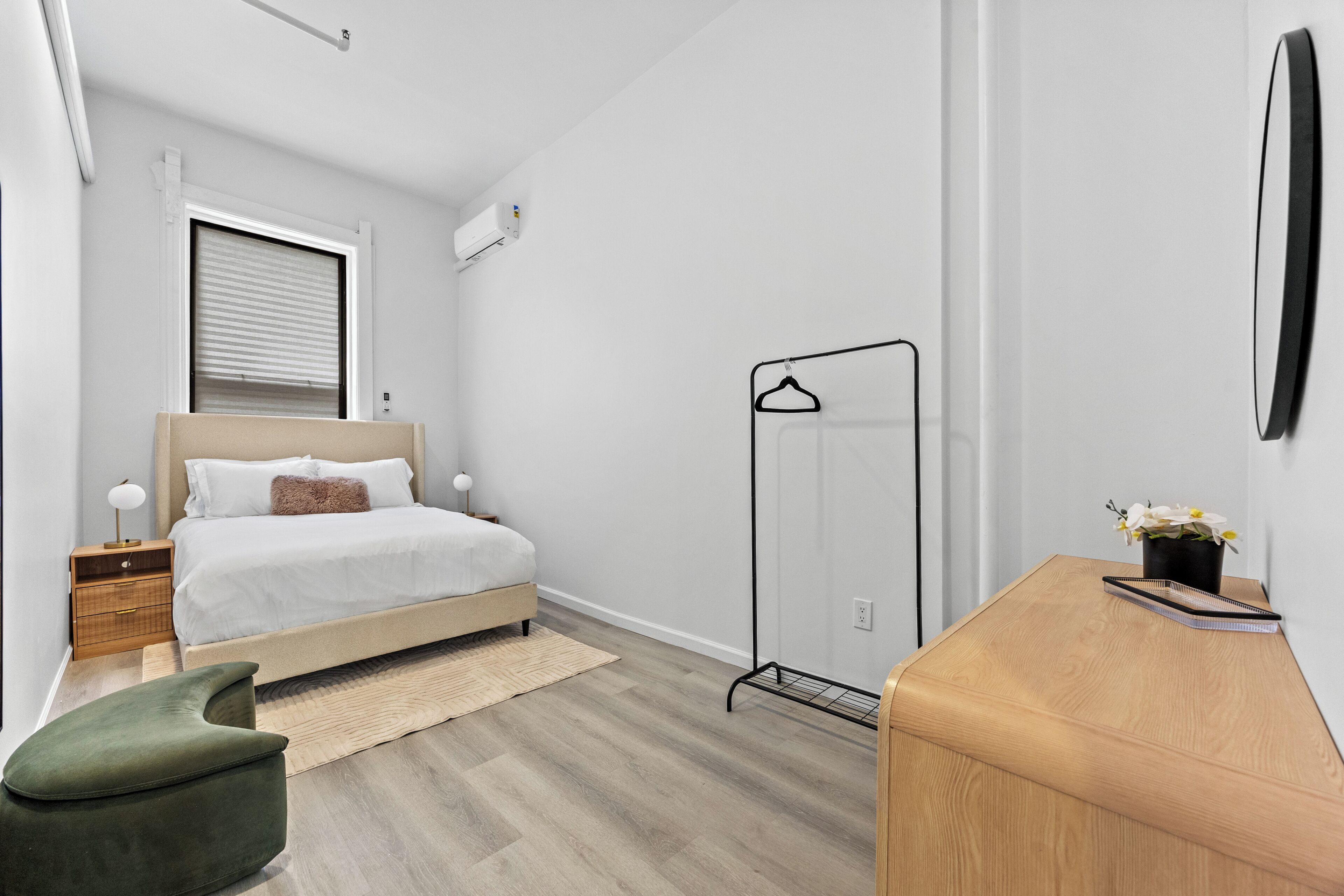 A modern bedroom with a bed, bedside tables, a hanging clothes rack, a desk, and a chair.