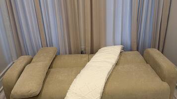 A sofa with a quilted cushion in a room with patterned carpet and sheer curtains.