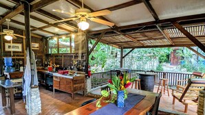 Una cocina rústica con armarios de madera y encimera de piedra, un comedor con mesa y sillas de madera, y un balcón con barandilla que da a zonas verdes.