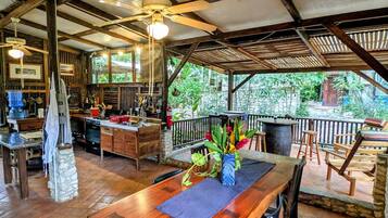 Une cuisine rustique avec des meubles en bois et un plan de travail en pierre, un coin repas avec une table et des chaises en bois, et un balcon doté d'une balustrade donnant sur un espace verdoyant.