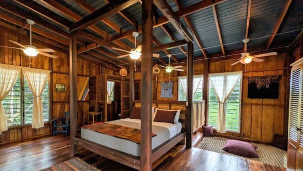 Una cabaña de madera con una cama grande, ventiladores de techo y vistas al exterior.