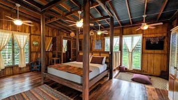 Une cabane en bois avec un grand lit, des ventilateurs de plafond et une vue sur l’extérieur.
