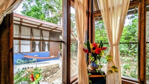 Una habitación con ventanas amplias, una estructura de madera en el exterior y un jarrón con flores sobre una mesa.