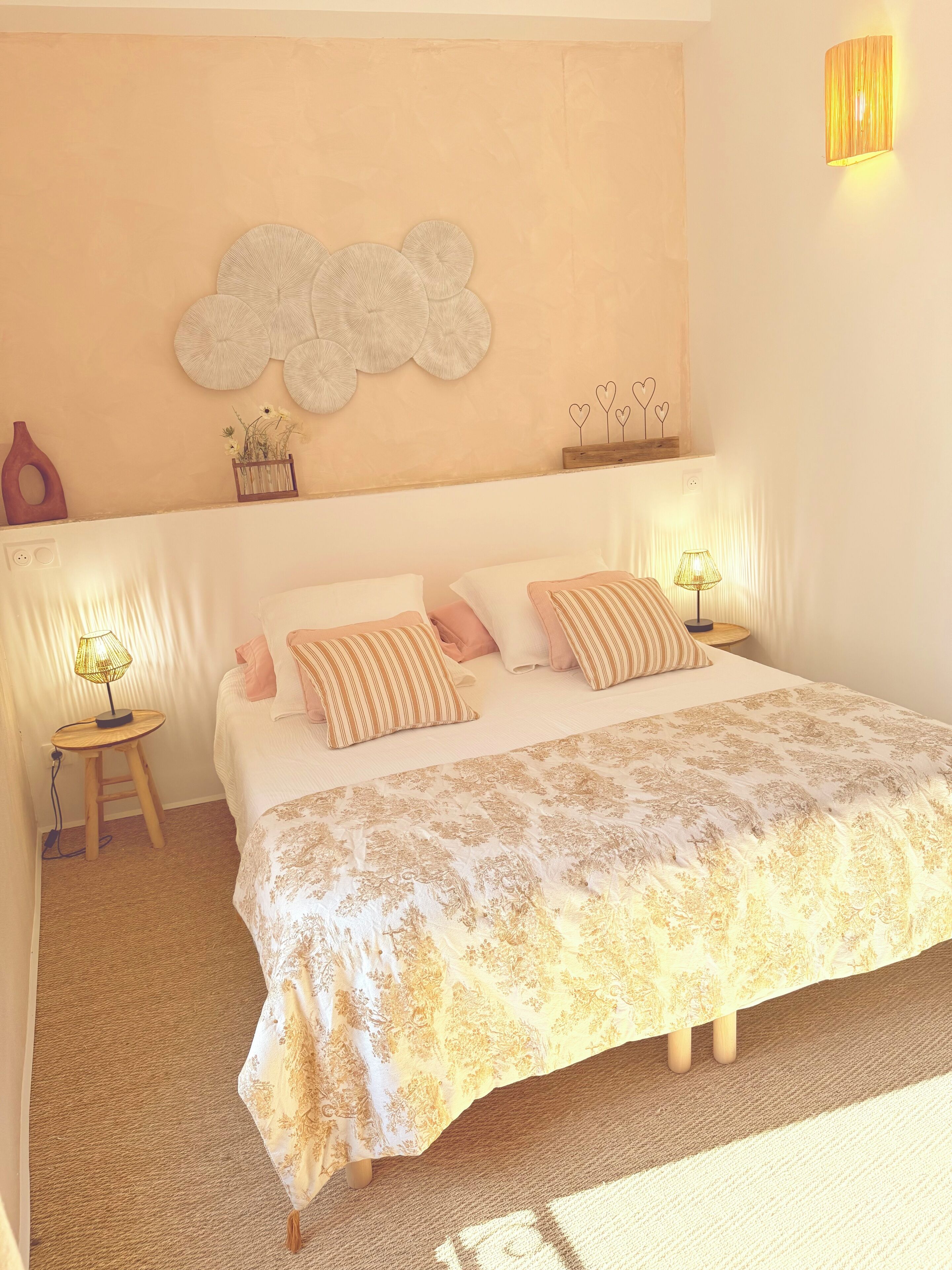 A bedroom with a large bed, two bedside lamps, a decorative wall piece, and a small table with a lamp.