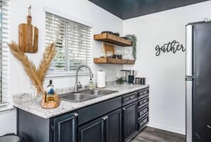 Una cocina moderna con gabinetes oscuros, encimera de granito, refrigerador de acero inoxidable y una ventana con persianas.
