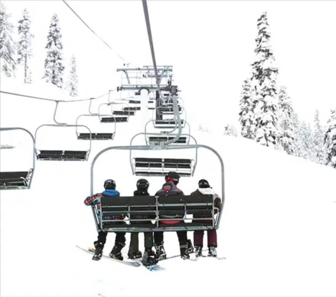 Een skilift met verschillende mensen erop, omgeven door met sneeuw bedekte bomen.