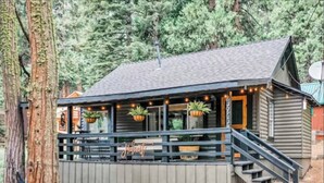 A rustic cabin with a wooden exterior, a balcony with hanging plants, and a staircase leading to the entrance. - The Hide-Out! A Boho Cabin AC- Wi-fi (Mi-Wuk Village)