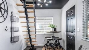 A modern interior with a spiral staircase, a round table with chairs, a potted plant, and a black door. - The Hide-Out! A Boho Cabin AC- Wi-fi (Mi-Wuk Village)