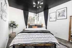 Un dormitorio con cama, una planta colgante y dos cuadros en la pared.