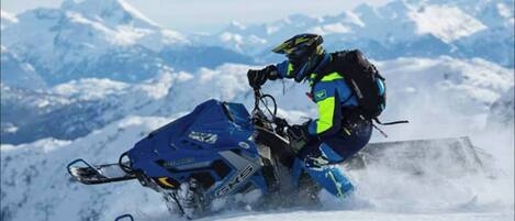 Una persona montando en moto de nieve, vestida con equipo azul y amarillo, sobre una montaña nevada.