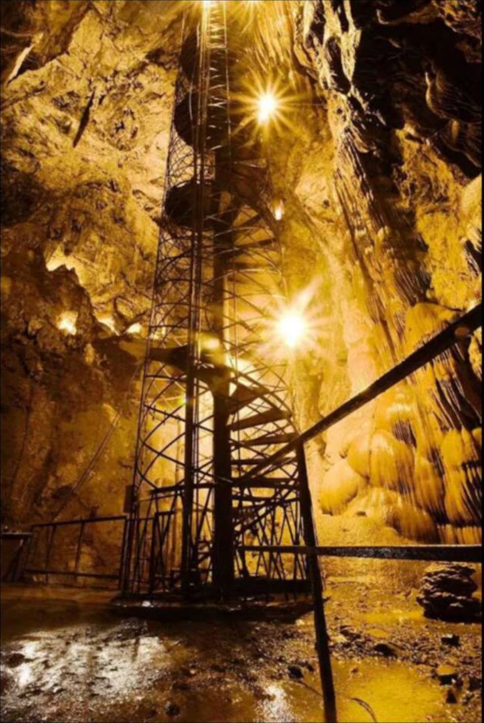 A metal structure in a cave with a ladder, surrounded by rocky walls and illuminated by artificial lights.