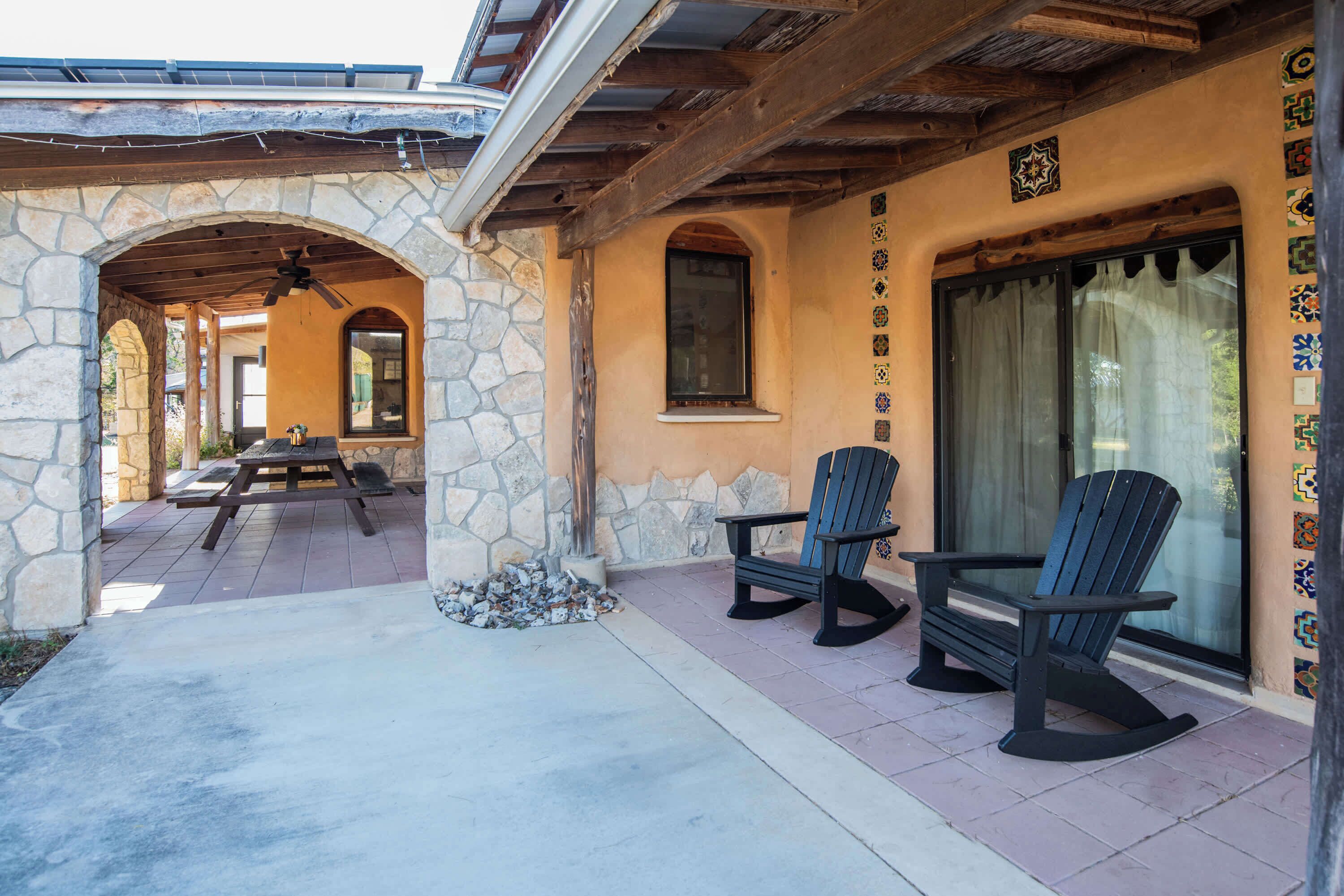 A covered patio area with stone walls, wooden beams, and a stone bench.