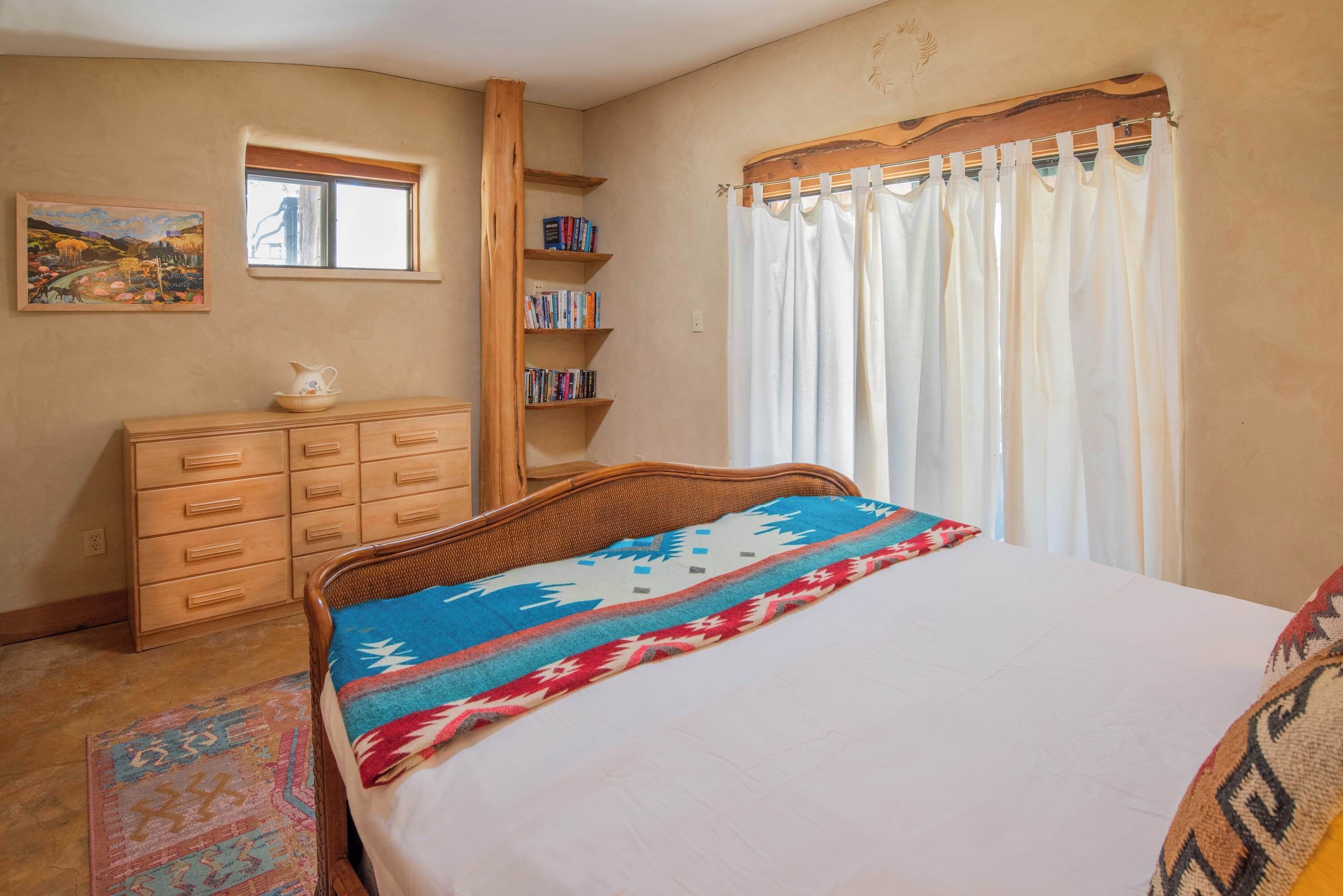 Une chambre à coucher avec un lit, une commode en bois, une bibliothèque, une fenêtre et un rideau.