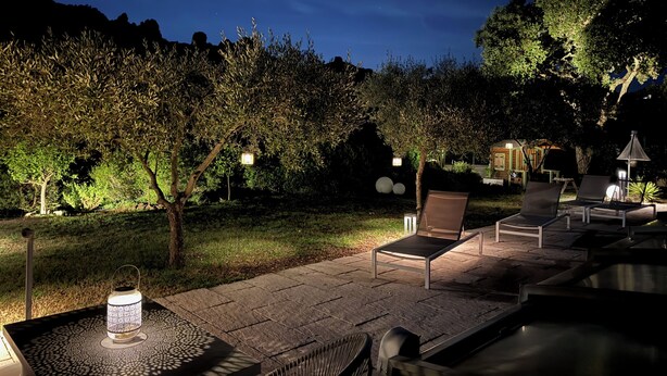 Ein Terrassenbereich im Freien mit Sitzgelegenheiten und Tisch, umgeben von Bäumen und Blick auf den Nachthimmel.