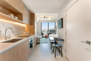 Eine moderne Küche mit Holzausbau, einer Edelstahlspüle und einem eingebauten Backofen. Ein Essbereich mit Tisch und Stühlen lädt zum Verweilen ein, und große Fenster bieten einen Blick auf die Stadt.