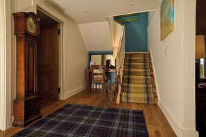A hallway with a wooden floor, a plaid rug, a grandfather clock, a chair, a staircase with a striped cushion, and a painting on the wall. - Luxury Island Living in the Heart of Gigha (Isle of Gigha)