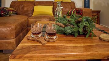 A wooden table with two glasses of amber liquid, a bottle, and a pine branch decoration.