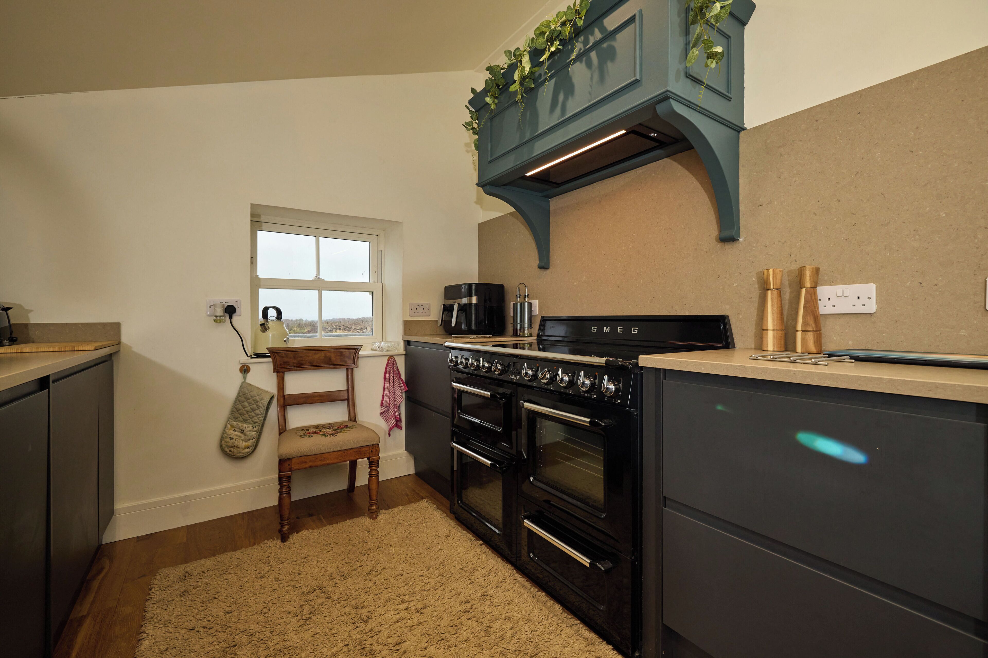 A kitchen with a built-in stove, oven, and coffee maker. There is a window, a chair, and a countertop with a plant.