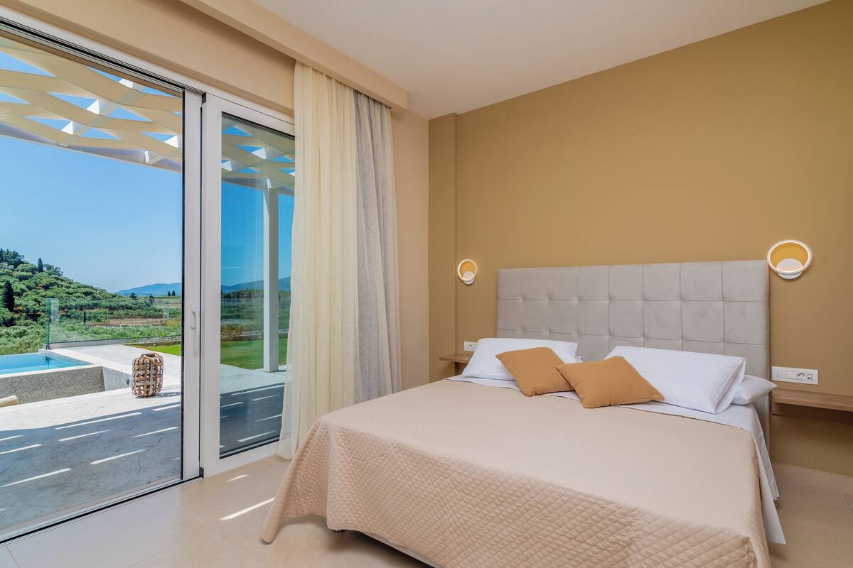 A bedroom with a large bed, a view of a pool and greenery, and a sliding glass door.