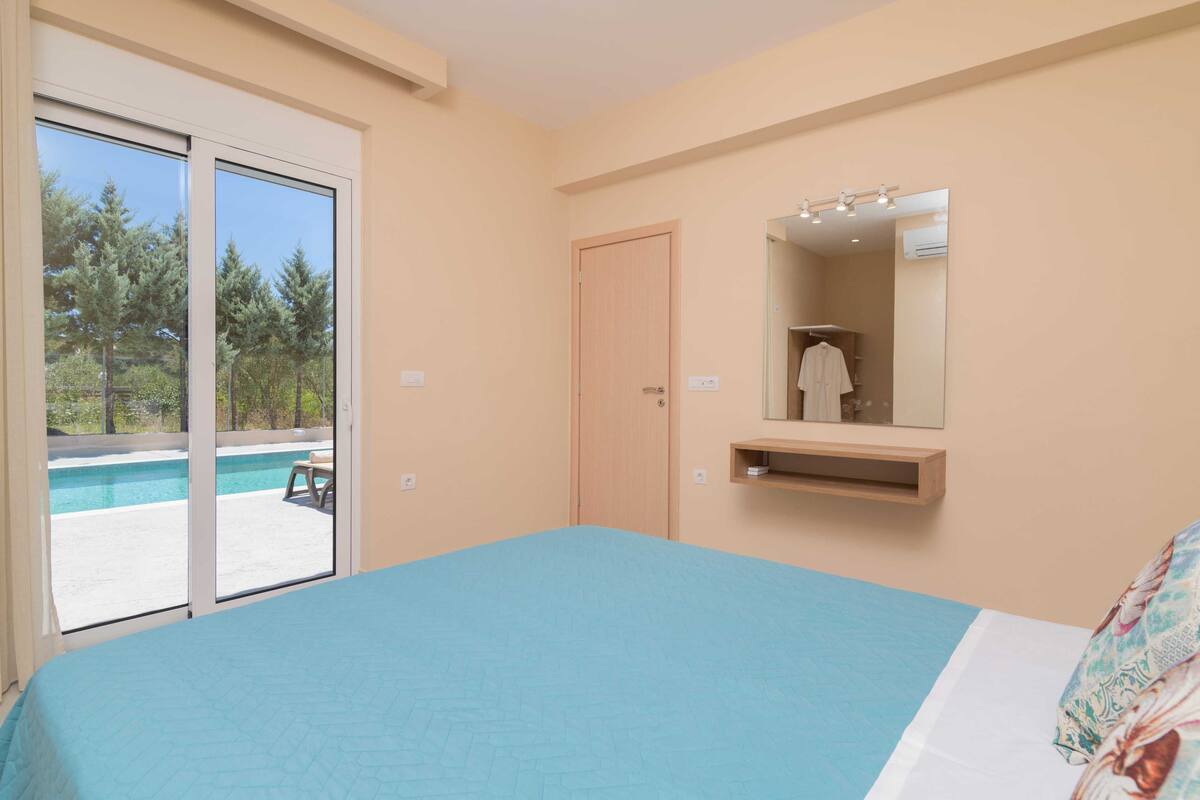 A bedroom with a large bed, a sliding glass door to a pool area, a wooden door, and a mirror above a shelf.