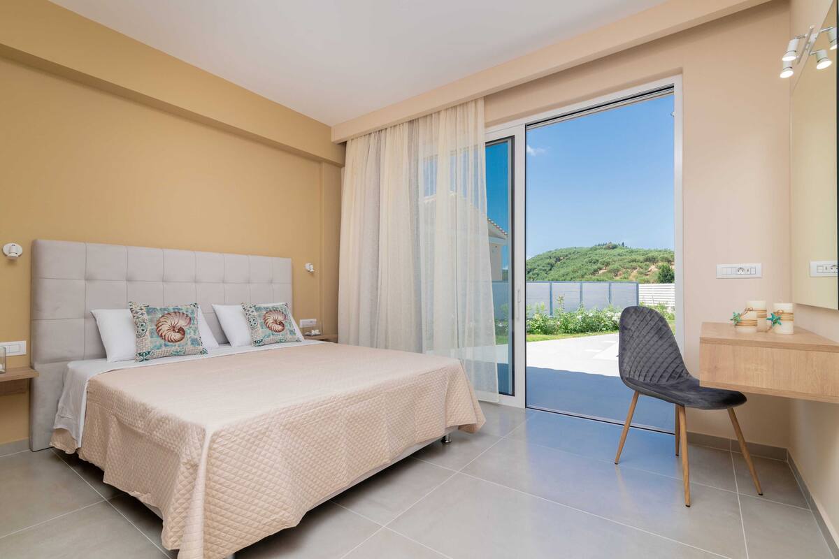 A bedroom with a bed, a chair, a desk, and a sliding glass door leading to a balcony.