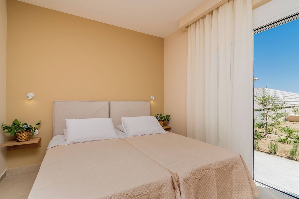 A bedroom with a large bed, two bedside tables with lamps, a window with curtains, and a view of the outside.