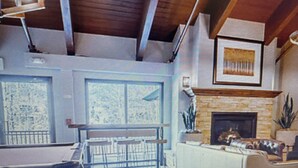 A modern living room with a fireplace, a dining area, and a staircase leading to an upper level. - Charming 1-bedroom condo in Vail. Complimentary shuttle to ski lift 1 mile away. (Vail)