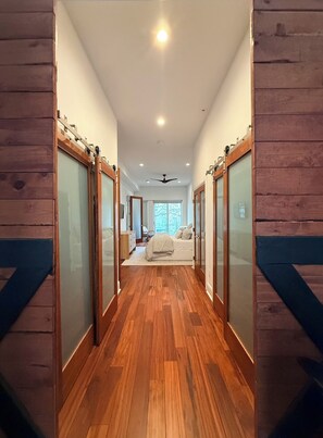 Um corredor com piso de madeira que dá para um quarto com cama e cômoda.