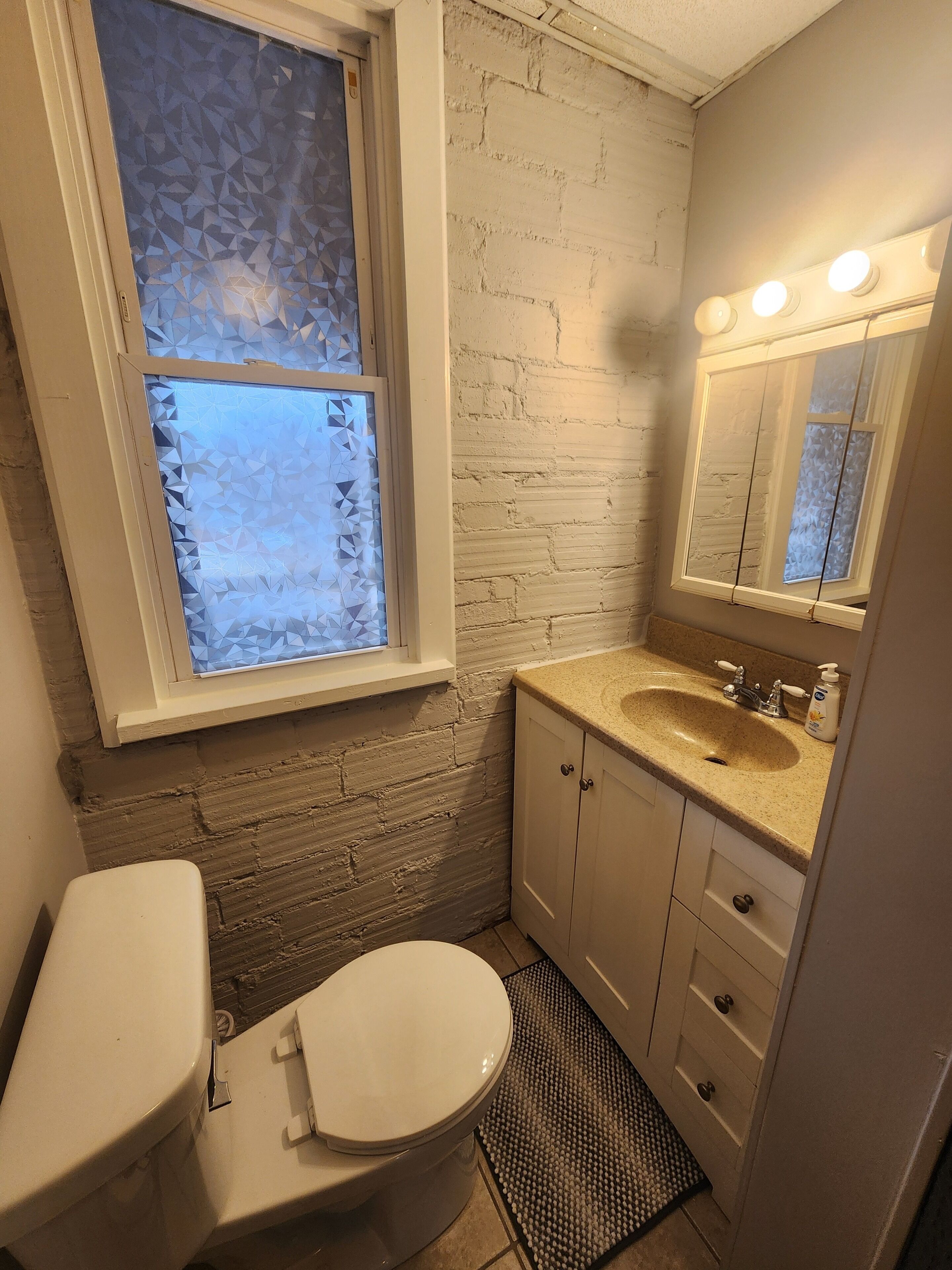 A bathroom with a white toilet, a sink with a mirror above it, and a window with frosted glass.