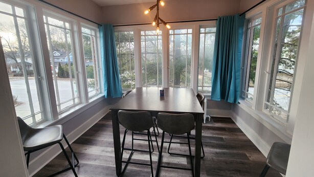 Un espace repas comprenant une grande table et des chaises, de grandes fenêtres avec des rideaux et un luminaire au plafond.