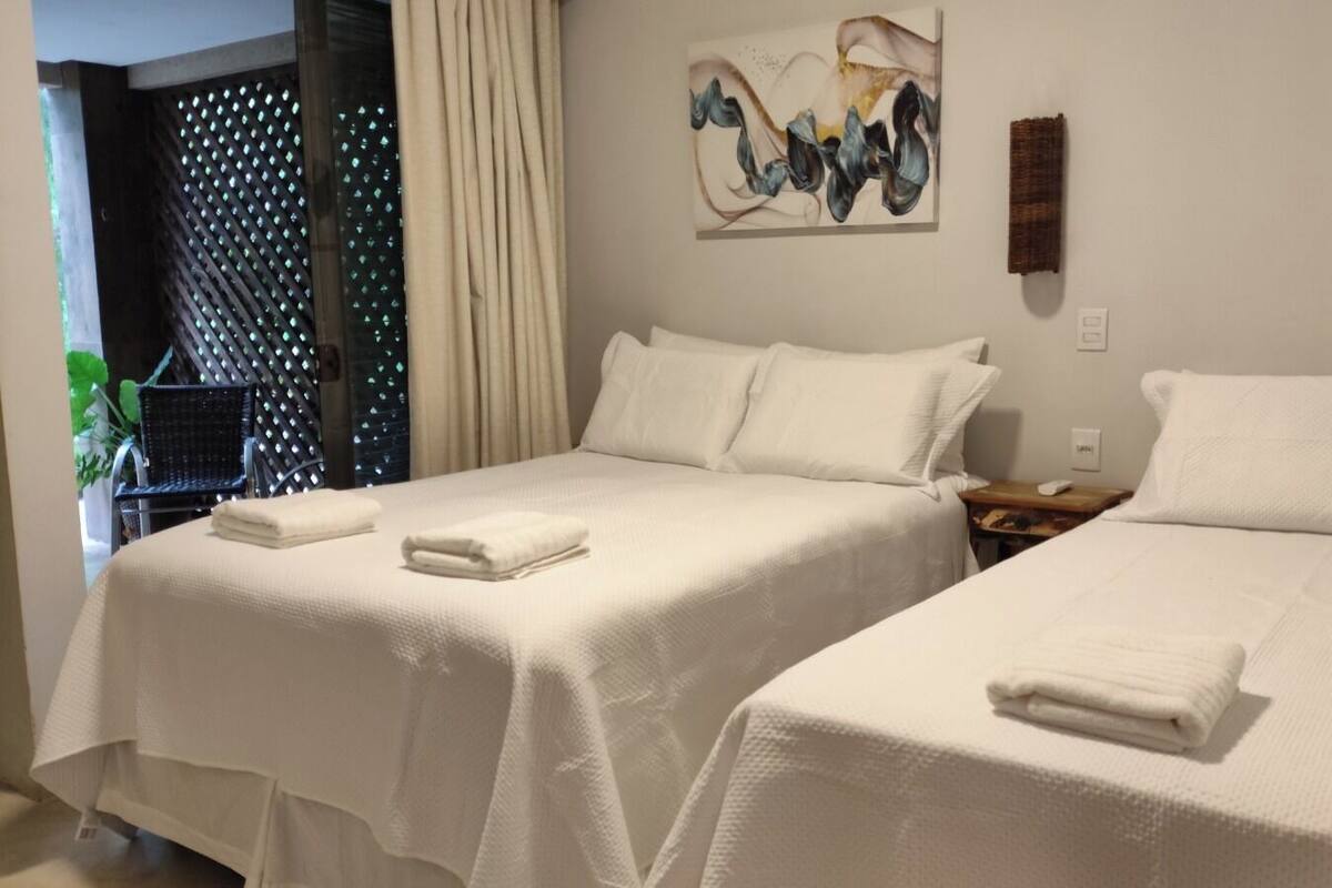 A hotel room with two beds, a painting on the wall, and a window with curtains.