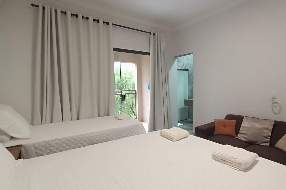 A hotel room with two beds, a sofa, and a balcony with curtains.