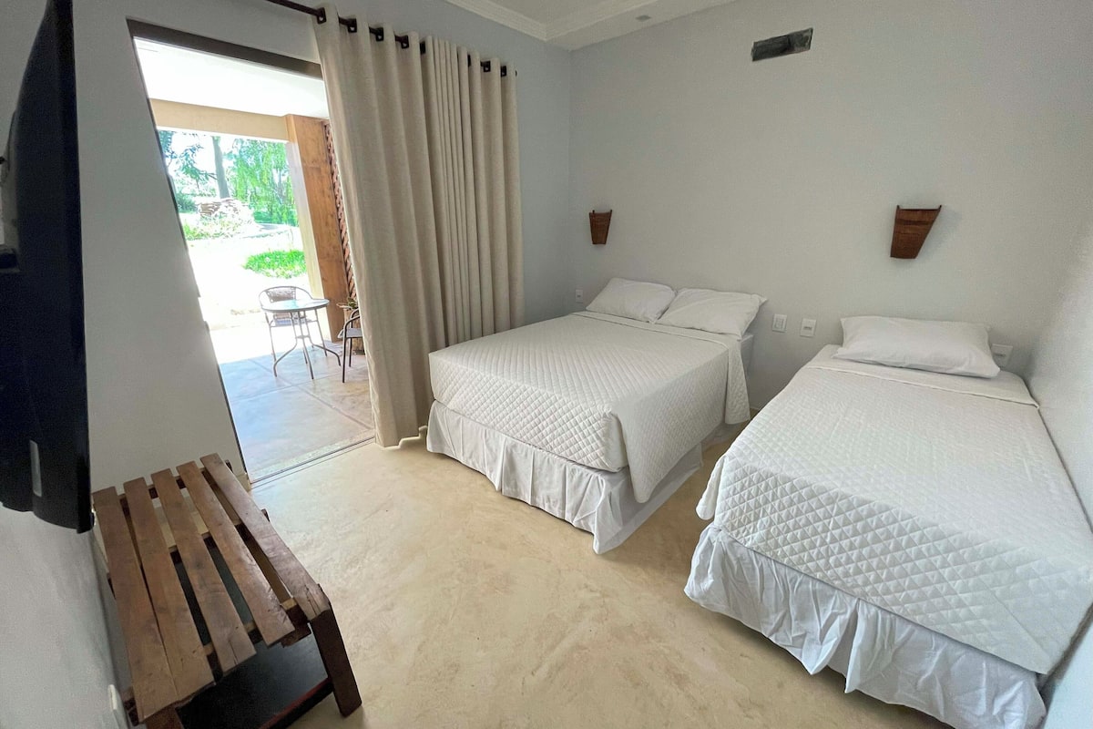 A hotel room with two beds, a wooden bench, and a view of the outdoors.