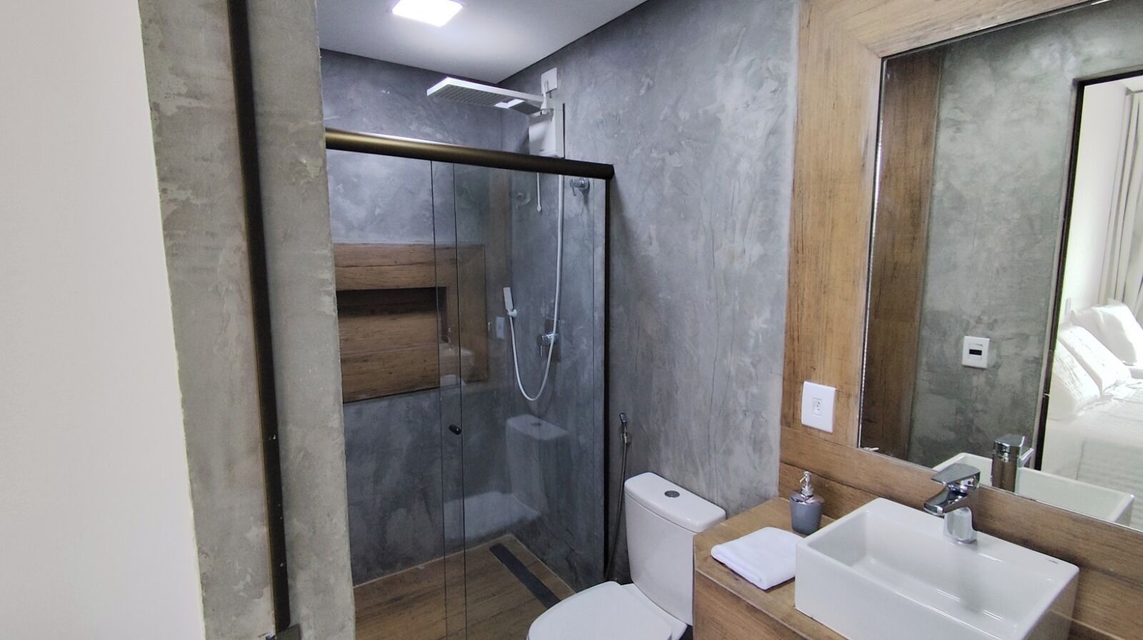 A modern bathroom with a glass-enclosed shower, a toilet, and a sink with a mirror.