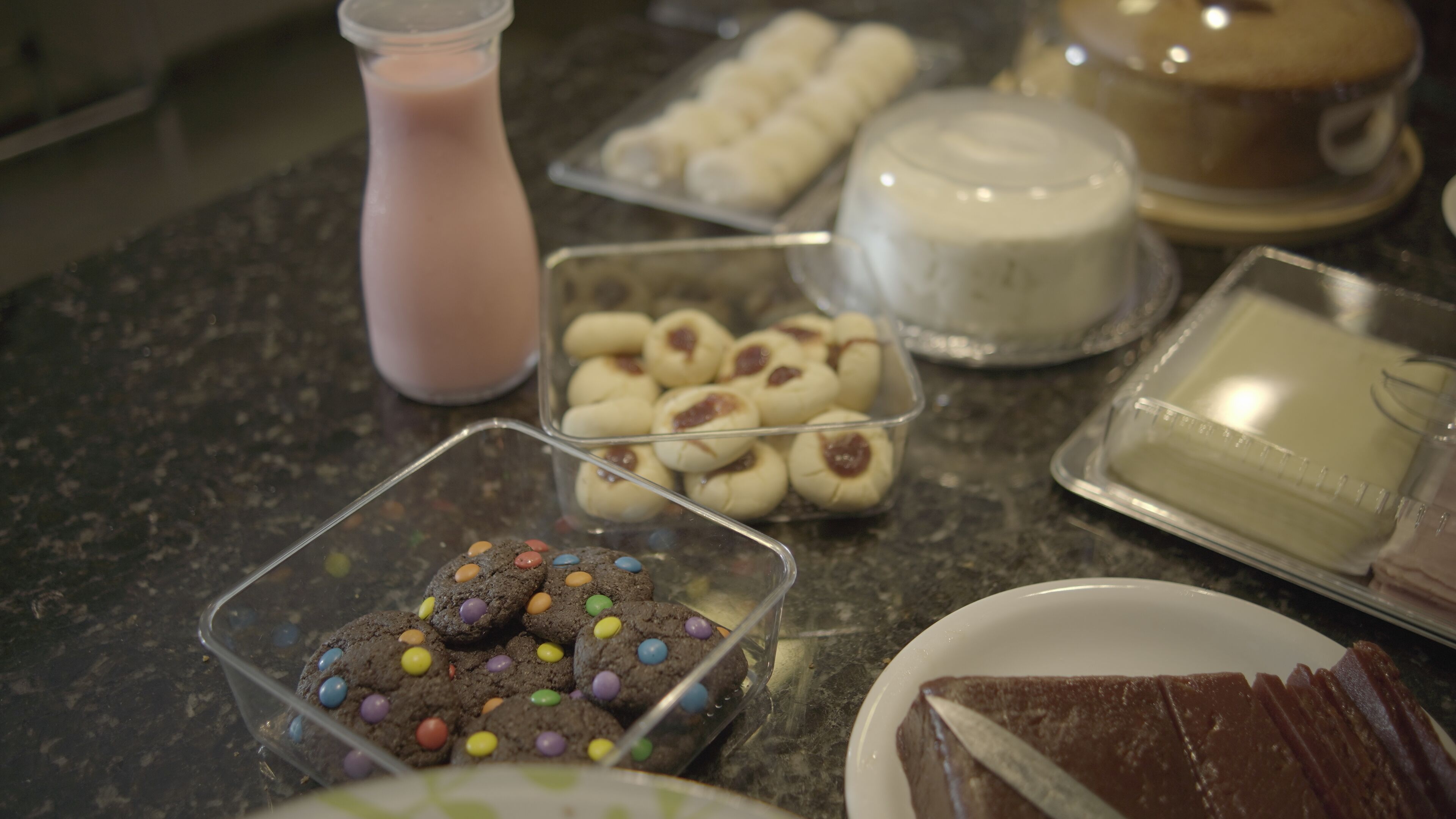 A variety of desserts including cookies, a cake, and a milk drink on a countertop.