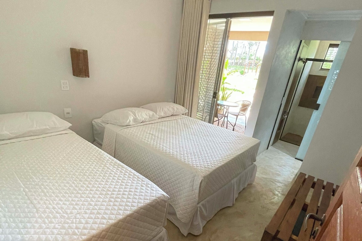 A hotel room with two beds, a wooden bench, and a sliding glass door leading to a balcony.