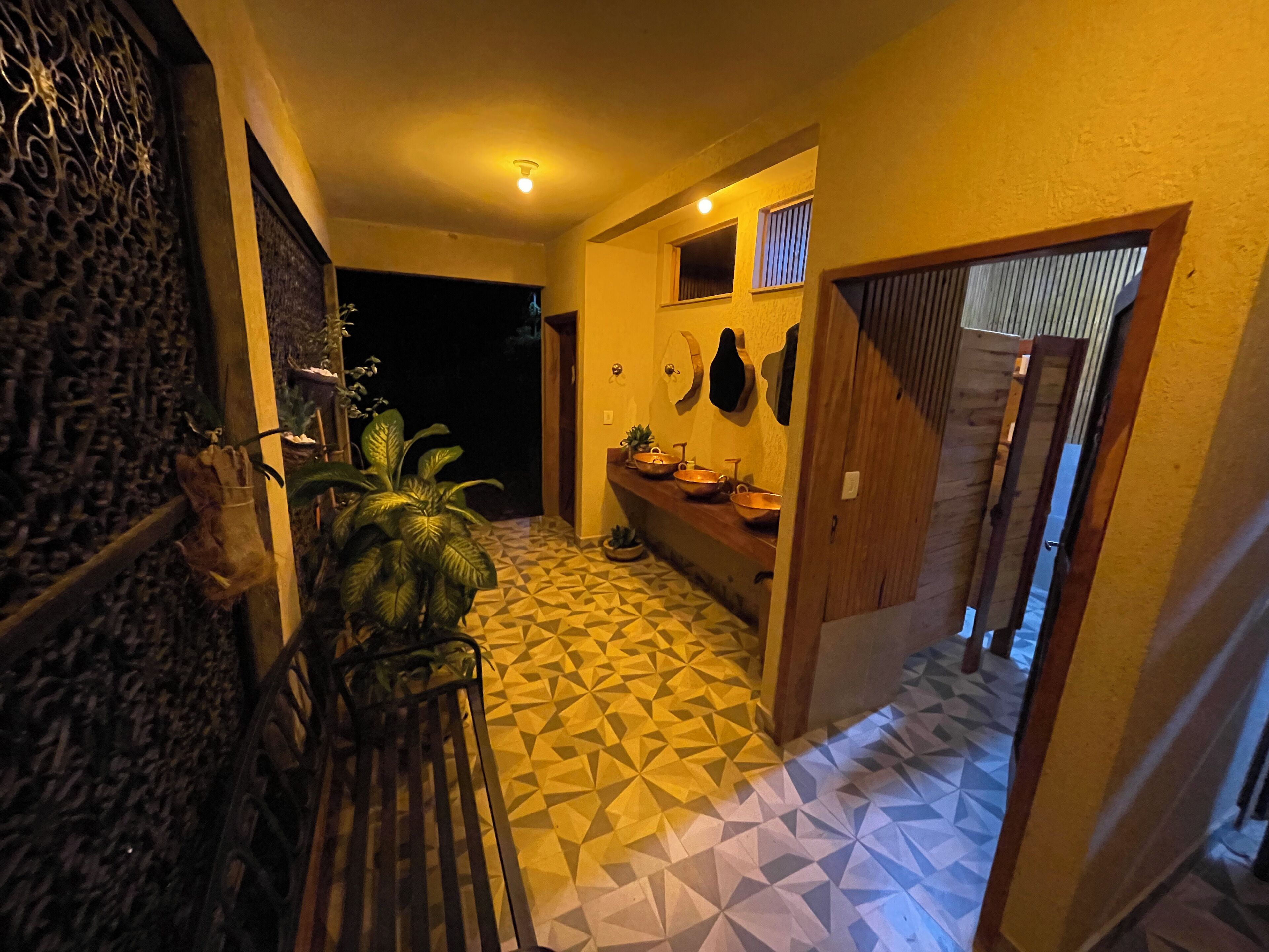 Un couloir doté d’un sol à motifs, d’un banc en bois, d’une plante en pot et d’un lavabo agrémenté de bols décoratifs.